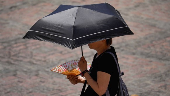 epa10710665 A woman uses a fan and protects herself from the sun with an umbrella in Cordoba, Spain, 25 June 2023. The current anticyclonic situation in Spain has led to the first heat wave of the sum ...
