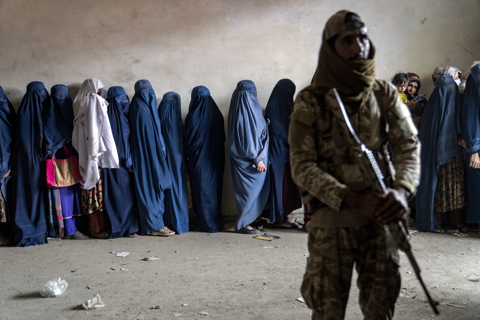 A Taliban fighter stands guard as women wait to receive food rations distributed by a humanitarian aid group in Kabul, Afghanistan, Tuesday, May 23, 2023. (AP Photo/Ebrahim Noroozi)
