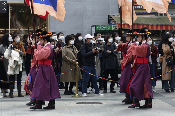 People wearing face masks watch a re-enactment ceremony of the changing of the Royal Guards, in front of the main gate of the Deoksu Palace in Seoul, South Korea, Friday, Nov. 13, 2020. South Korea ha ...
