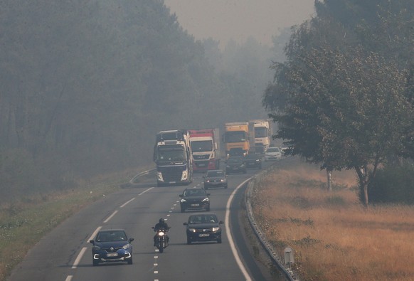 Trucks and cars drive on the A63 motorway invaded by smoke caused by the forest fire fifty km south of Bordeaux, near Belin-Béliet, southwestern France, Monday, July 18, 2022. France scrambled more wa ...
