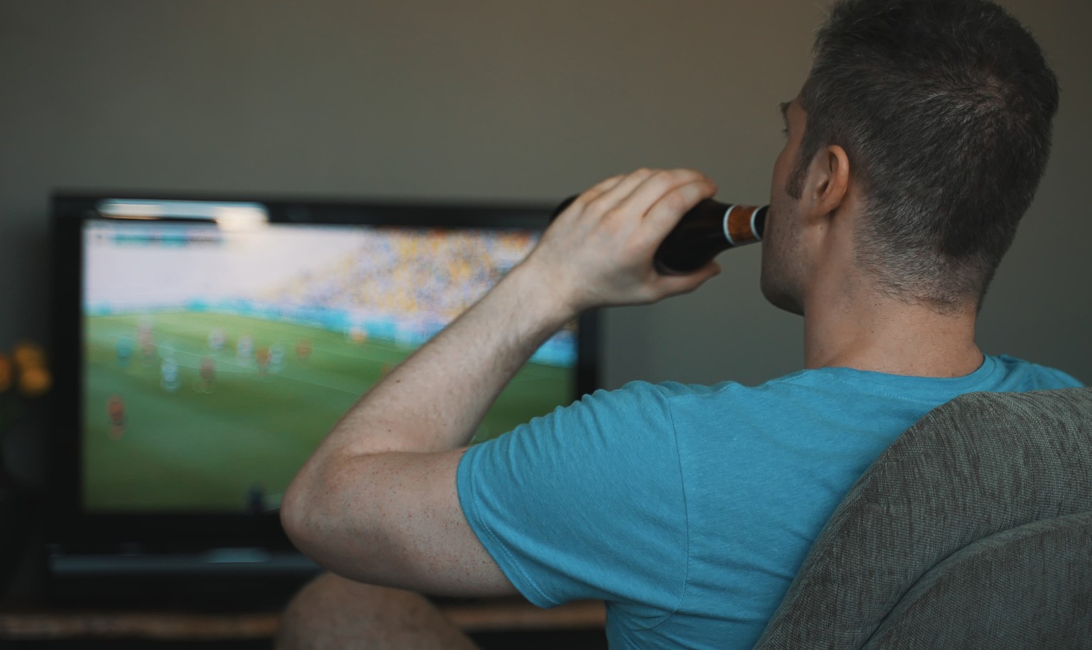Man with bottle of beer watching football on TV.