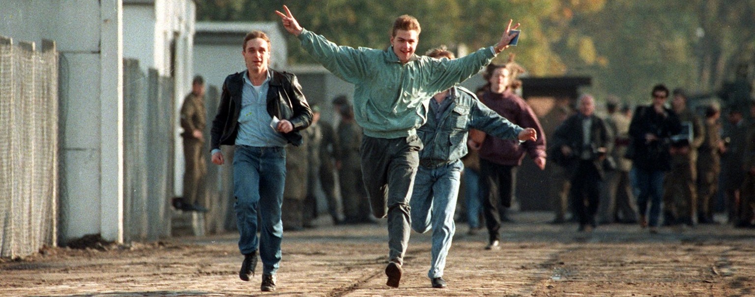 Jubelnd laufen drei junge Ost-Berliner am 10. November 1989 durch einen Berliner Grenzuebergang. Der Untergang des SED-Regimes hatte sich in einem rasanten Tempo vollzogen: Unter dem Druck der Bevoelk ...