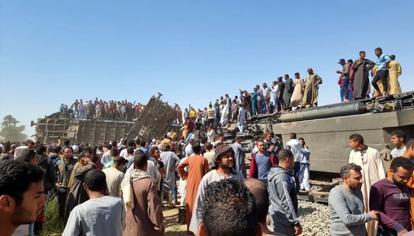 epa09099059 People stand atop a turned over train carriage as others inspect the scene of a train crash in Sohag province, Egypt, 26 March 2021. At least 32 people were killed and some 66 injured as t ...