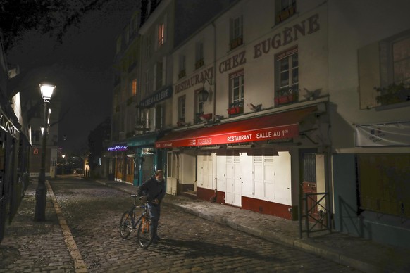FILE - In this Dec. 15, 2020 file photo, a man pushes his bicycle along a row of closed restaurants in Montmartre, during the new imposed curfew in Paris. Trying to fend off the need for a third natio ...