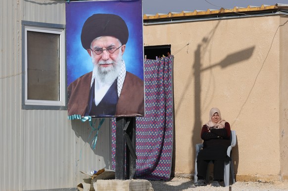 epaselect epa12636509 A refugee woman sits next to a portrait of Iranian Supreme Leader Ayatollah Ali Khamenei outside her makeshift shelter at the Imam Ali Complex in Hermel, Bekaa Valley, near the b ...