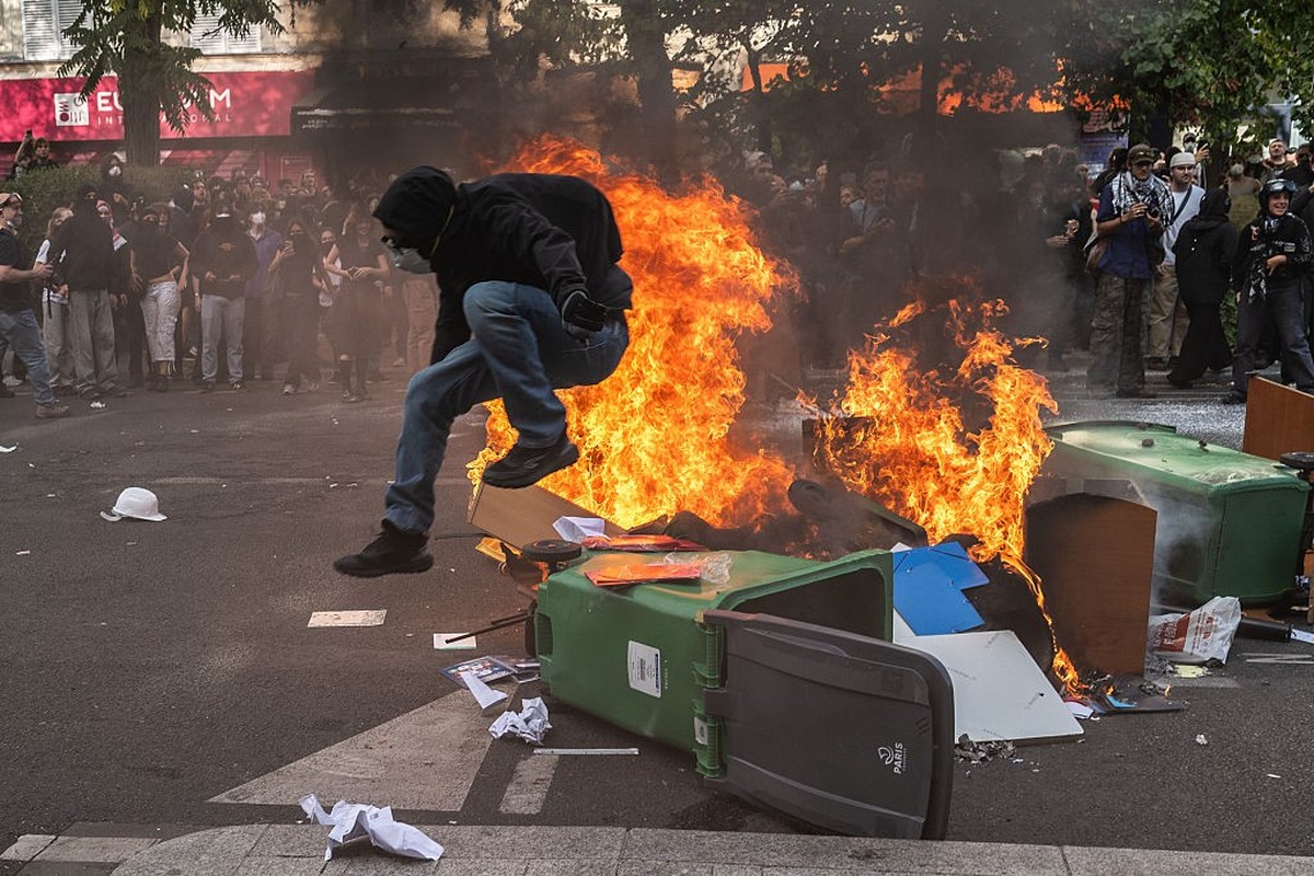 PARIS, FRANCE - OCTOBER 6: A protestor jumps over a wheelie bin as a fire is started on Voltaire boulevard while tens of thousands of secondary school students and their supporters march from Republic ...