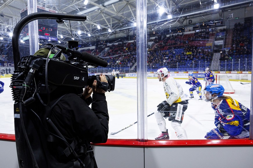 Ein SRF TV Kameramann filmt durch die Plexiglas-Scheibe das Eishockey-Meisterschaftsspiel der National League zwischen den Teams EHC Kloten und HC Ajoie am Samstag, 2. Dezember 2023, in Kloten. (KEYST ...