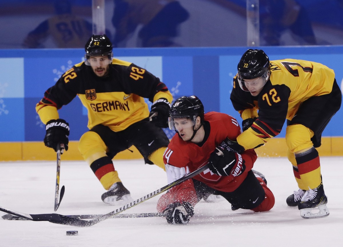 Yasin Ehliz, of Germany, left, and teammate Dominik Kahun, right, fights for control of the puck with Pius Suter, of Switzerland, center, during the first period of the qualification round of the men& ...