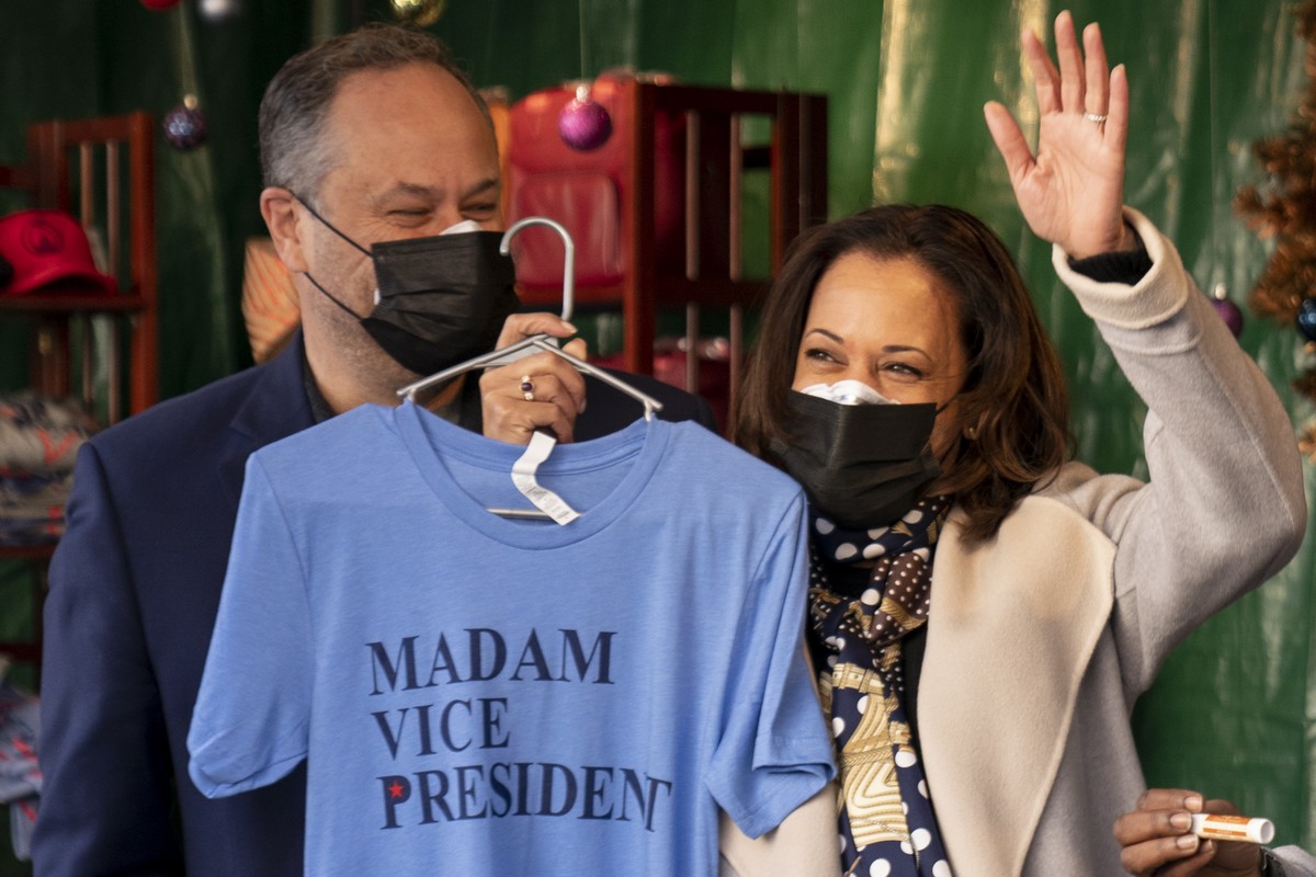 Vice President-elect Kamala Harris, accompanied by her husband Doug Emhoff, left, holds up a shirt that reads "Madam Vice President" as they visit the "made in DC" booth in the Dow ...