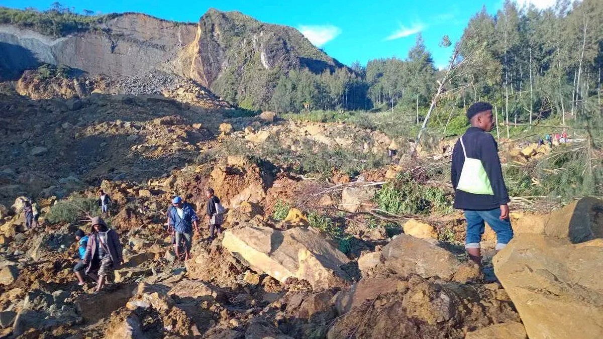 epa11365145 People walk with their belongings in the area where a landslide hit the village of Kaokalam, Enga province, Papua New Guinea, 24 May 2024. A landslide reportedly killed about 100 people in ...
