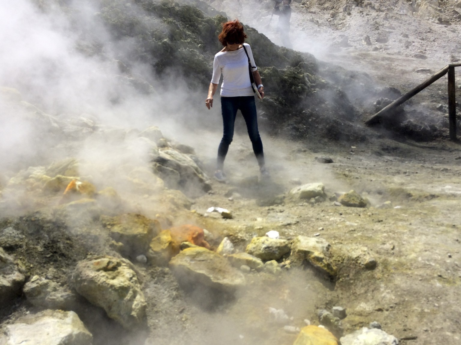 In this photo taken on Saturday, April 30, 2016, a woman takes a close look at a steaming fumarola in the Solfatara crater bed, in the Phlegraean Fields near Naples, Italy.  Fields -- Campi Flegrei in ...