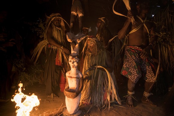 NGOUNIé PROVINCE, GABON - 2024/08/17: Participants in a Bwiti ceremony, dressed in ritual attire made from dried palm fronds, dance with lit torches inside a small temple near the totem pole. Bwiti is ...