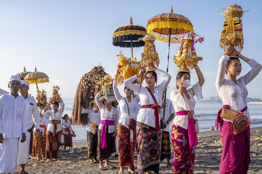 epa10531276 Balinese Hindu people wear 'Pratima', or a symbol of God, as they walk on a beach during a cleansing ceremony called 'Melasti', in Denpasar, Bali, Indonesia, March 19…