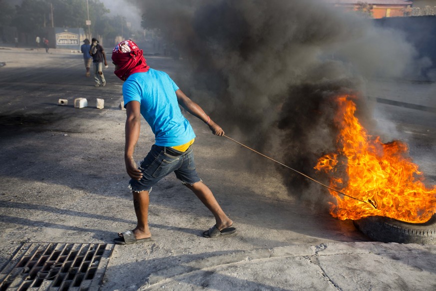 A protester pulls a burning tire in the middle of the street during a protest over the cost of fuel in Port-au-Prince, Haiti, Saturday, July 7, 2018. Major protests erupted Friday in Haiti as the gove ...