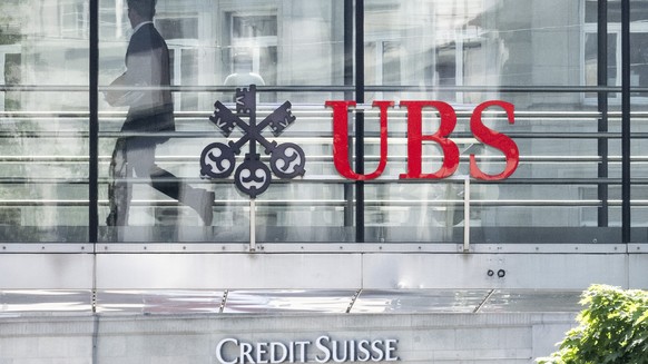 Ein Mann laeuft zwischen den beiden Logos der Banken UBS und Credit Suisse, aufgenommen am Montag, 12. Juni 2023 in Zuerich. Heute verkuendete die nunmehr einzige Schweizer Grossbank in einem offenen  ...