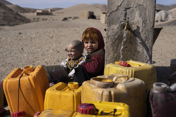 Two Afghan children sit next to a spigot as people of Kamar Kalagh village outside Herat, Afghanistan, try to fill their plastic containers with water, on Friday, Nov. 26, 2021. Afghanistan