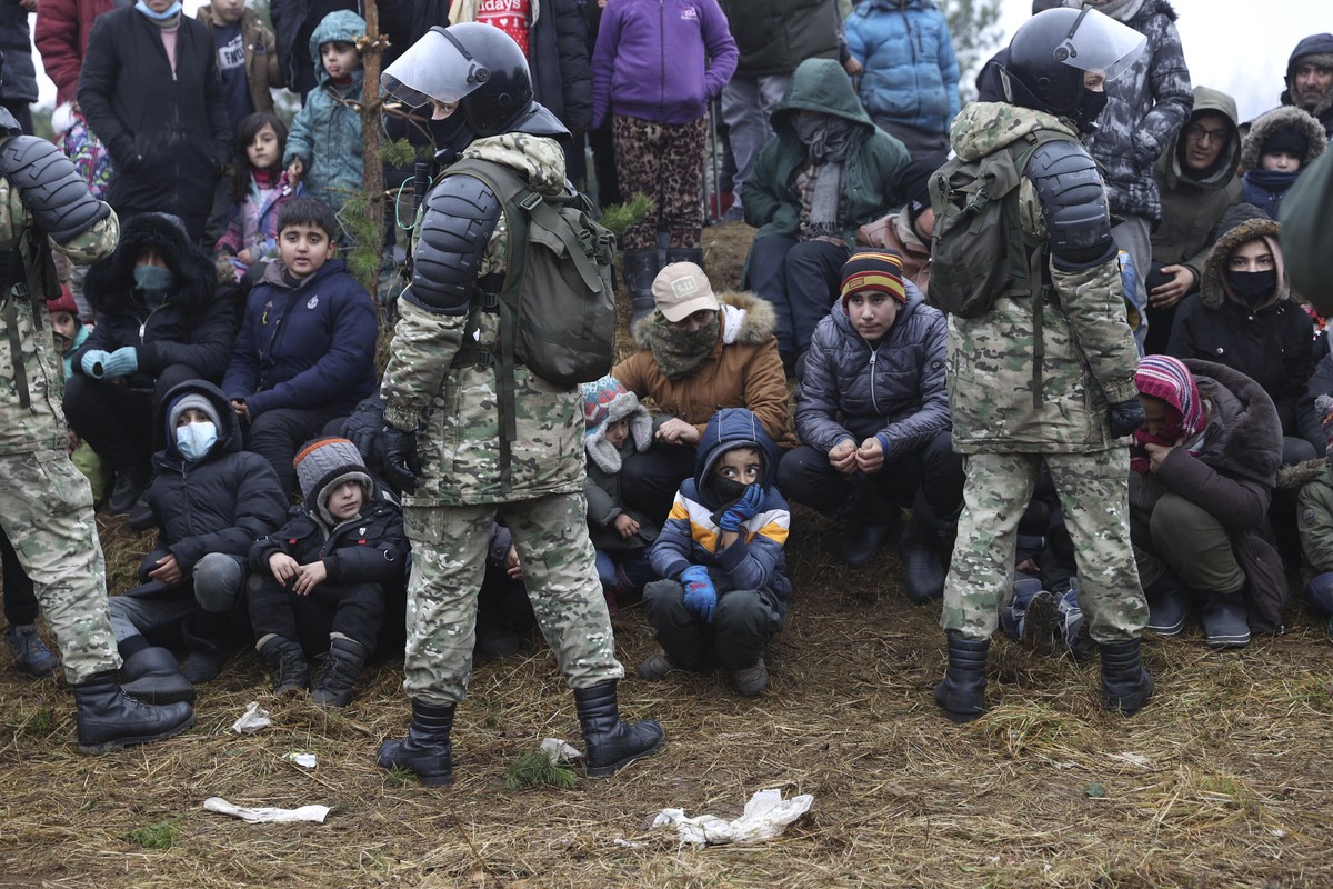 Migrants from the Middle East and elsewhere stand in front of Belarusian servicemen as they gather at the Belarus-Poland border near Grodno, Belarus, Sunday, Nov. 14, 2021.Poland's prime minister ...