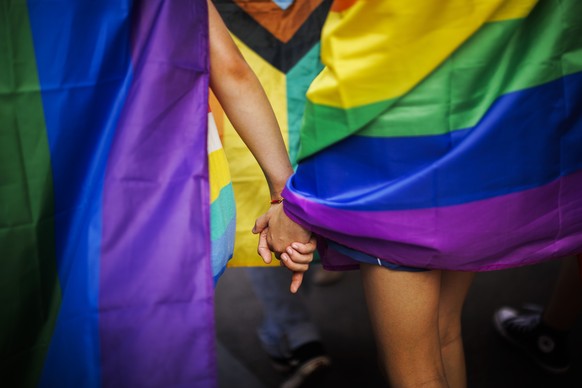 Two women wearing rainbow colored flags hold hands, during the Zurich Pride parade in Zurich, Switzerland, Saturday, June 18, 2022. (Michael Buholzer/Keystone via AP)