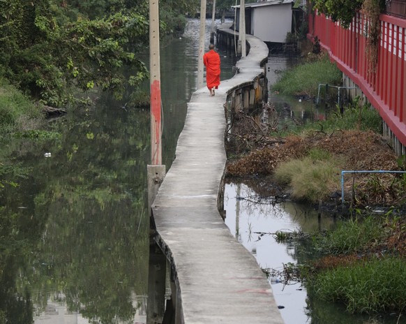 epa05177758 A Buddhist monk dressed in traditional orange colored robes walks along an elevated cement footpath above one of the Thai capital&#039;s many canals, passing the reflection in the water of ...