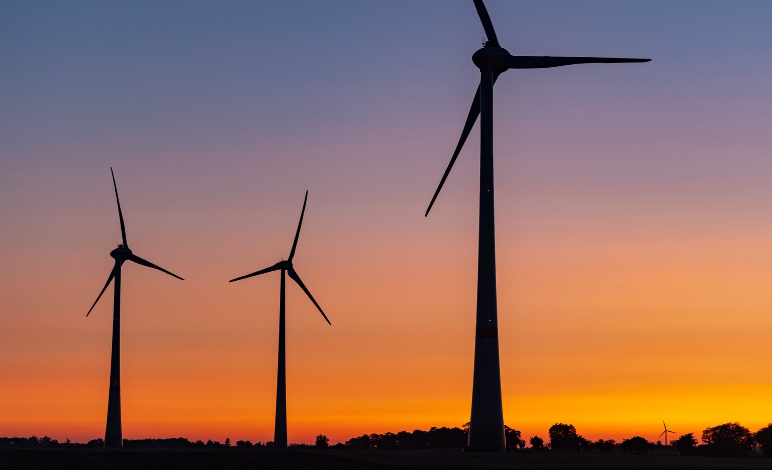 Windraeder sind vor einem farbenpraechtig leuchtenden Morgenhimmel kurz vor Sonnenaufgang zu sehen, am Freitag, 26. Juli 2019, in Mallnow, Deutschland. Auch am Freitag soll es vielerorts in Deutschlan ...