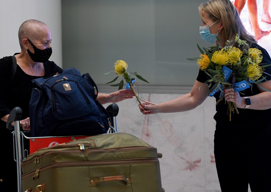 epa09556707 A traveller (left) arriving on the first quarantine free international flight is handed a native Australian flower by an airport worker at Sydney International Airport, in Sydney, Australi ...