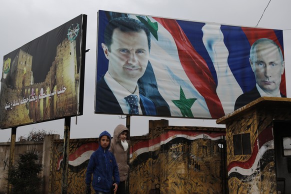 Syrian walk by posters of Syrian President Bashar Assad and Russian President Vladimir Putin in Aleppo, Syria, Thursday, Jan. 18, 2018. Syria said on Thursday its air defense would shoot down any Turk ...