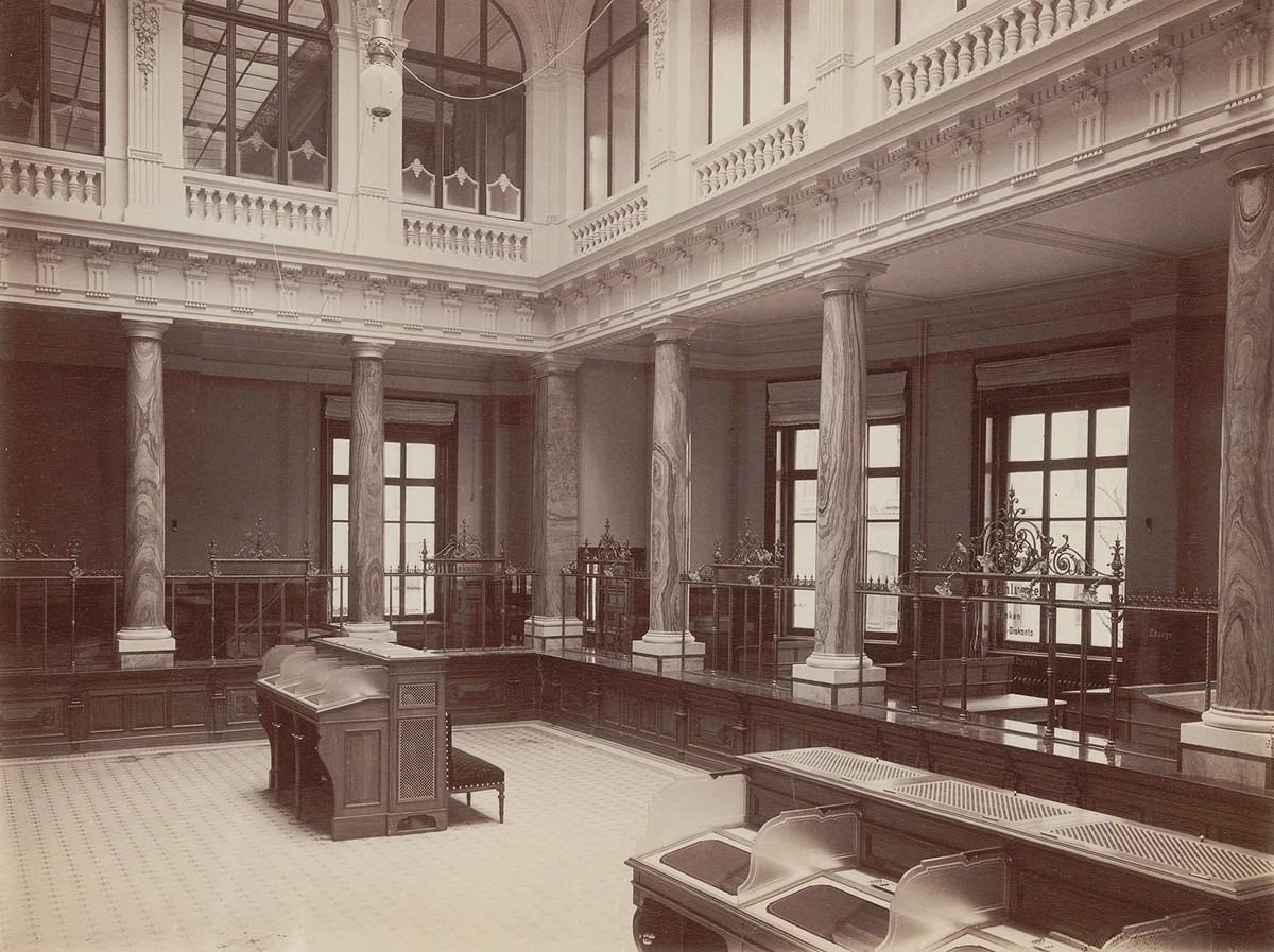Schalterhalle der Zürcher Kantonalbank in der oberen Bahnhofstrasse, um 1900. Zwischen den Säulen sind die Schalter angeordnet, in der Mitte befinden sich Schreibplätze für die Kundschaft.
https://www ...