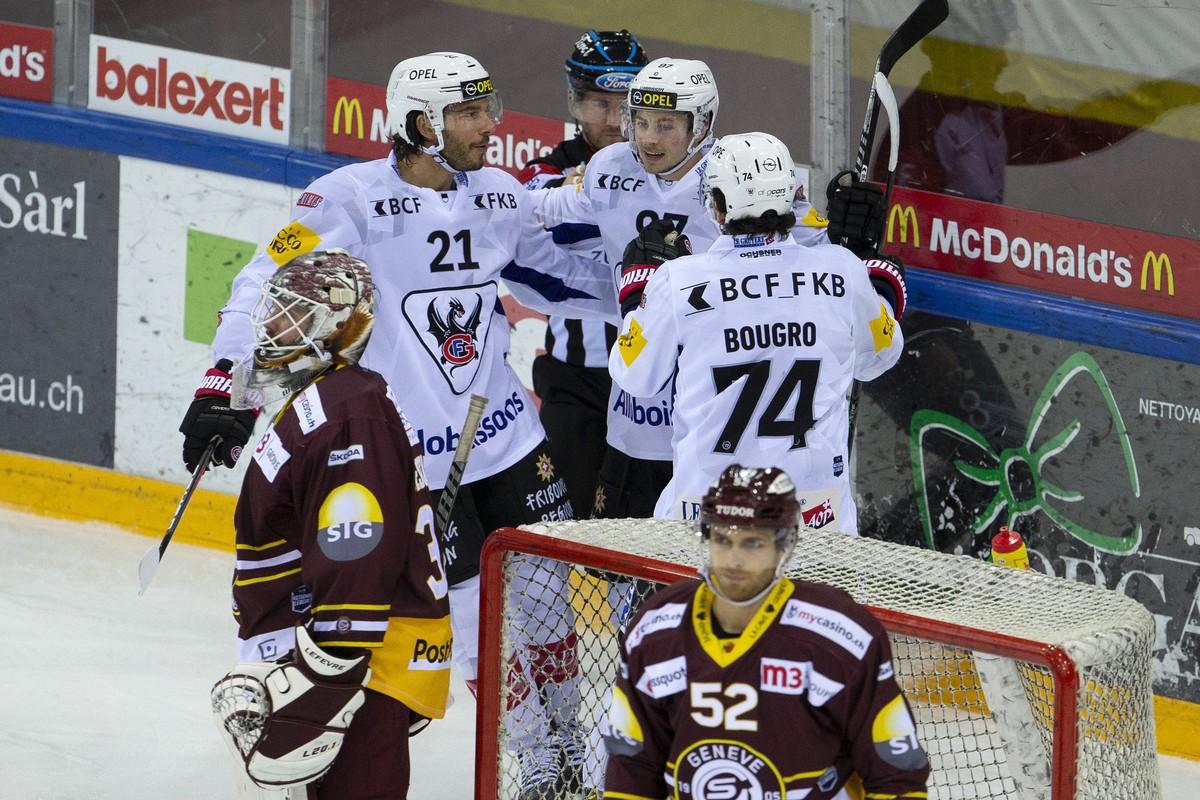 Fribourg's forward Nathan Marchon, center, celebrates his goal with teammates forward Mauro Joerg #21 and forward Jordann Bougro #74, of France, behind Geneve-Servette's goaltender Gauthier  ...