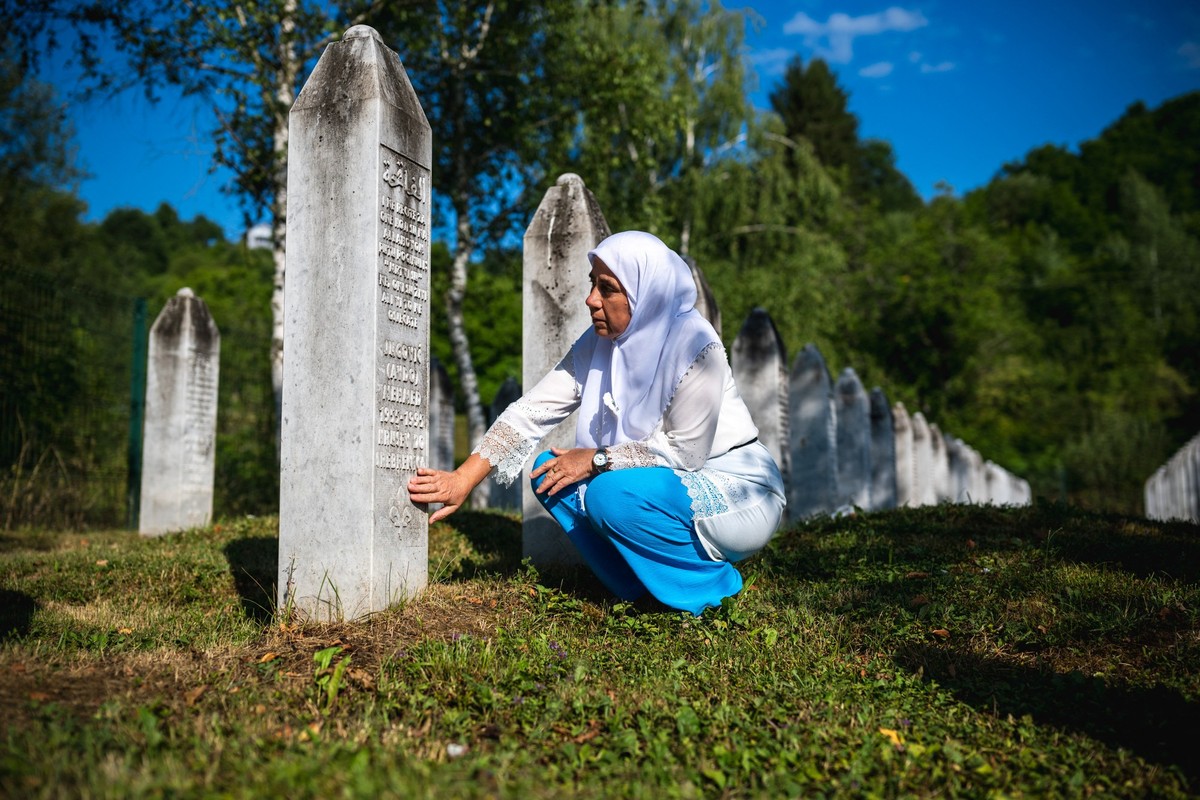 A woman touches a gravestone at the memorial cemetery in the village of Potocari, near the eastern Bosnian town of Srebrenica, on July 11, 2025, on the 30th anniversary of the Srebrenica massacre.