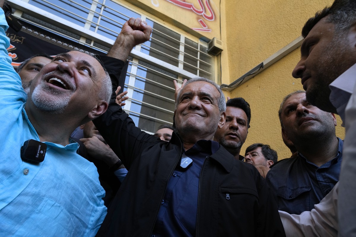 Reformist candidate for the Iran's presidential election Masoud Pezeshkian clenches his fist after casting his vote as he is accompanied by former Foreign Minister Mohammad Javad Zarif, left, at  ...