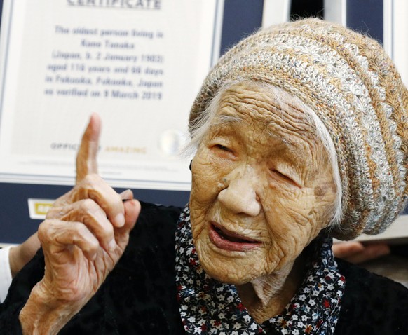 Kane Tanaka, a 116-year-old Japanese woman, gestures after receiving a Guinness World Records certificate, back, at a nursing home where she lives in Fukuoka, southwestern Japan, Saturday, March 9, 20 ...