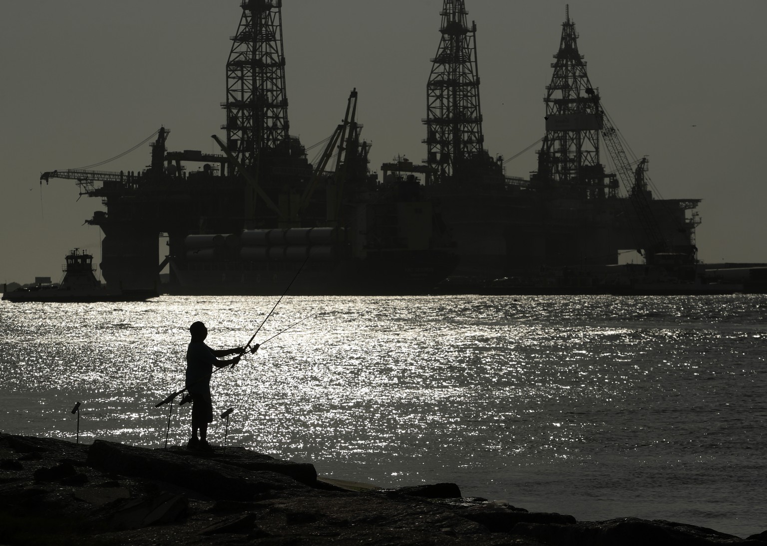 FILE - A man fishes near an oil drilling platform on May 8, 2020, in Port Aransas, Texas. Offshore oil and gas operations in the Gulf of Mexico are releasing far more climate-changing methane than off ...