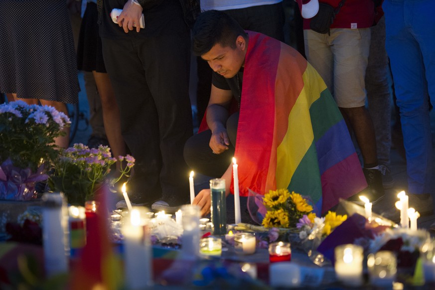 An unidentified man, wrapped in a Rainbow Flag, lights a candle during a vigil in Washington, Monday June 13, 2016, hosted by the Muslim American Women&#039;s Policy Forum, in memory of the victims of ...