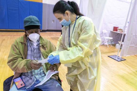 Registered Nurse Rita Alba points out to Beltran Orlando the return date on his vaccination card while he rests in the recovery area after his receiving the first dose of coronavirus vaccine at a pop- ...