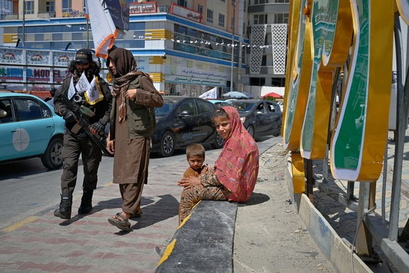A woman and child sit by the roadside as armed Taliban walk past during celebrations marking the fifth anniversary of the U.S. withdrawal from Afghanistan and the Taliban's return to power, in Ka ...