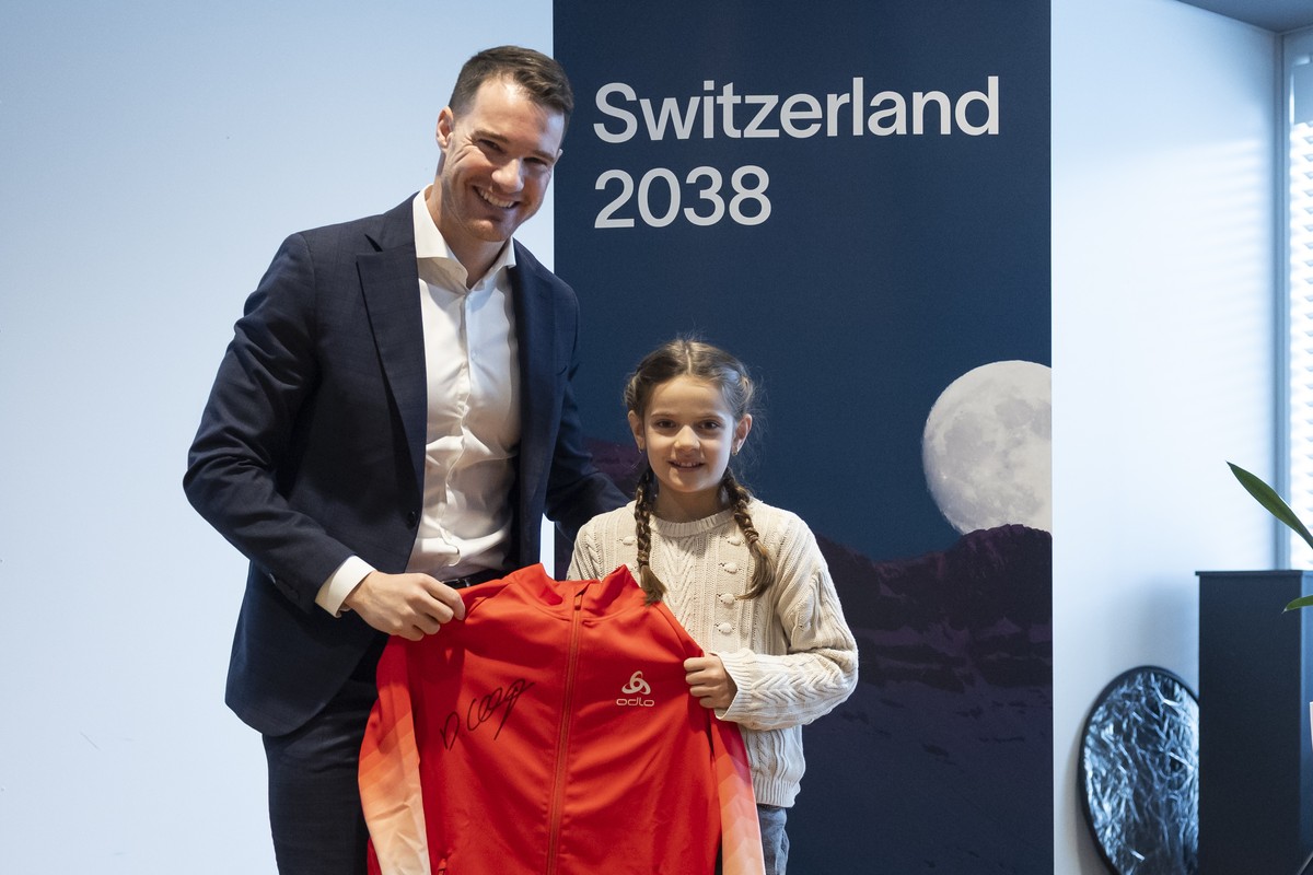 Dario Cologna, Vorstandsmitglied Switzerland 2038 und Vertreter der Athleten, uebergibt der jungen Langlauf-Athletin Malena Mueller eine Jacke, die er bei Olympia getragen hat, waehrend einer Medienko ...