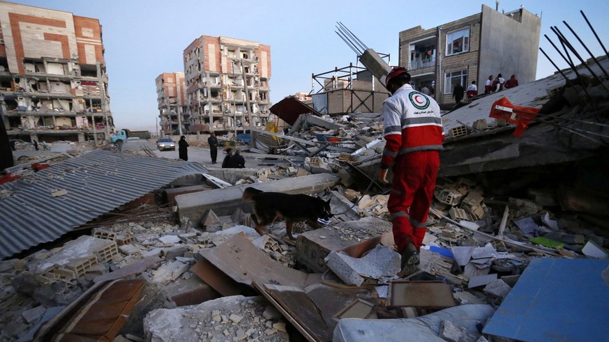 In this photo provided by the Iranian Students News Agency, ISNA, a rescue worker searches debris for survivors with his sniffing dog after an earthquake at the city of Sarpol-e-Zahab in western Iran, ...