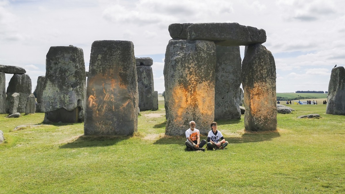 In this handout photo, Just Stop Oil protesters sit after spraying an orange substance on Stonehenge, in Salisbury, England, Wednesday June 19, 2024. (Just Stop Oil via AP)