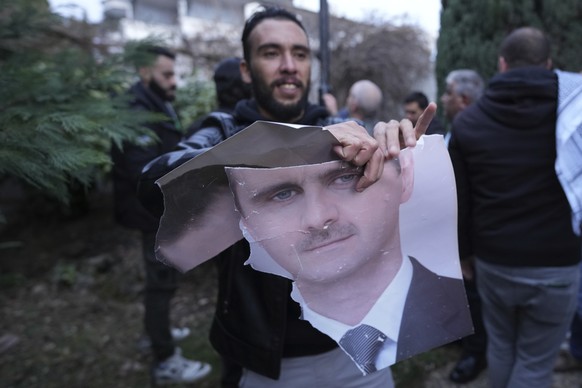 A man tears up a photo of Syrian President Bashar Assad in front of the Syrian embassy in Belgrade, Serbia, Sunday, Dec. 8, 2024. (AP Photo/Darko Vojinovic)