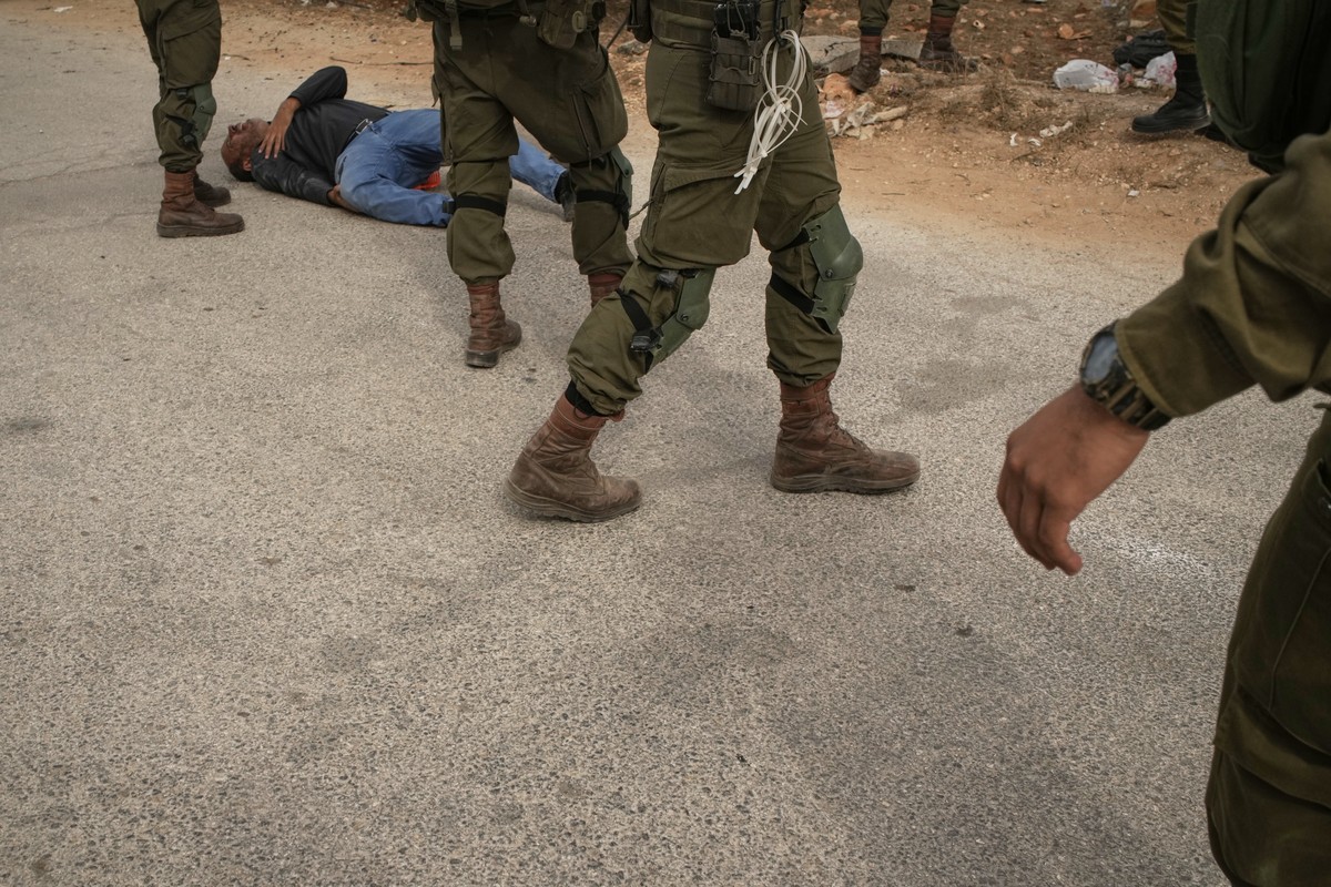 Israeli soldiers stand beside a wounded Palestinian man lying on a road after they shot him in the leg following a settler attack on Palestinians harvesting olives in the West Bank village of Abu Fala ...