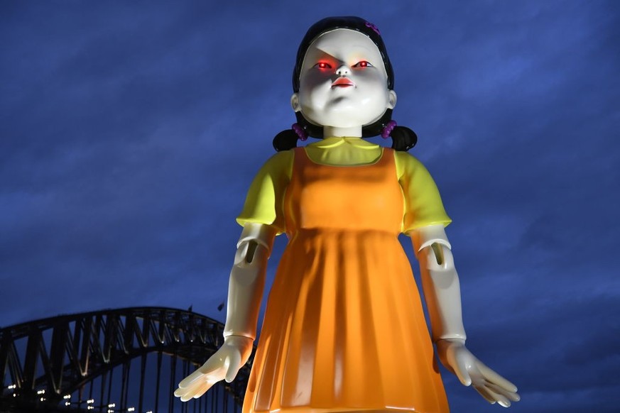 SYDNEY, AUSTRALIA - OCTOBER 30: A giant pigtailed doll with the Harbour Bridge in the background on October 30, 2021 in Sydney, Australia. The replica animated doll from the Netflix series Squid Game  ...