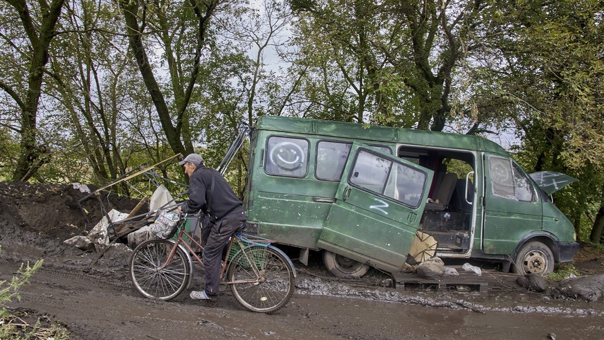 epa10182258 A local man rides a bicycle past a damaged car with the Z symbol on a road near the recently recaptured city of Balakliia in Kharkiv's area, Ukraine, 13 September 2022. The Ukrainian army  ...