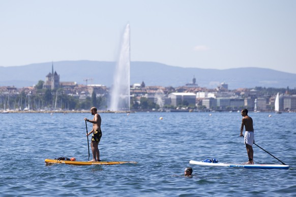 People paddle on their stand up paddle on Geneva Lake with the famous water fountain &quot;Le Jet d&#039;Eau&quot; and Cathedrale Saint Pierre are seen in background, in Cologny near Geneva, Switzerla ...