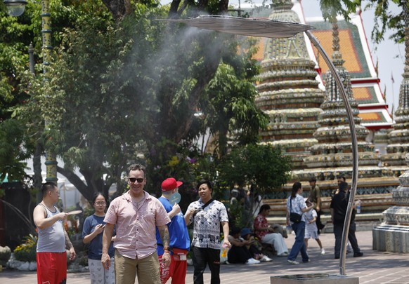 epa12889160 A tourist cools off by an irrigation sprinkler set up to cool down visitors during hot weather at Wat Pho temple or Temple of the Reclining Buddha in Bangkok, Thailand, 14 April 2026. The  ...
