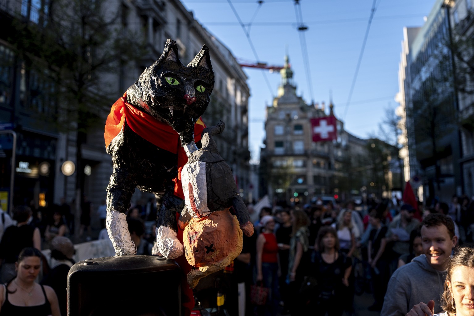 Eine Pappmache Katze haelt eine Figur von US-Praesident Donald Trump im Mund waehrend Personen an einer Demonstration gegen den Iran-Krieg der USA durch die Stadt ziehen am Mittwoch, 8. April 2026 in  ...