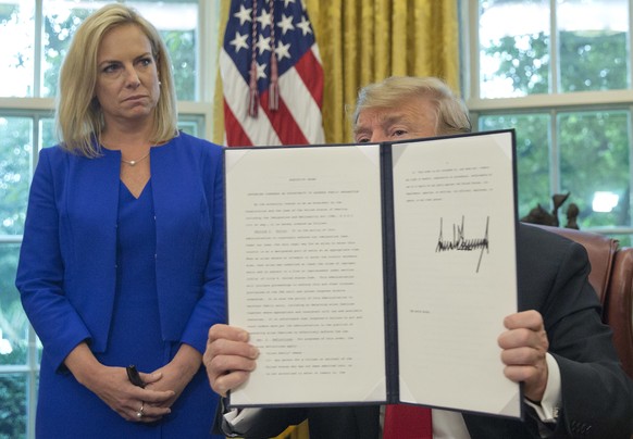 President Donald Trump holds up an executive order he signed to end family separations, during an event in the Oval Office of the White House in Washington, Wednesday, June 20, 2018. Looking on is Hom ...