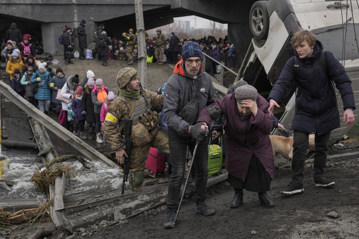 An elderly lady is assisted while crossing the Irpin river, under a bridge that was destroyed by a Russian airstrike, as civilians flee the town of Irpin, Ukraine, Saturday, March 5, 2022. What looked ...