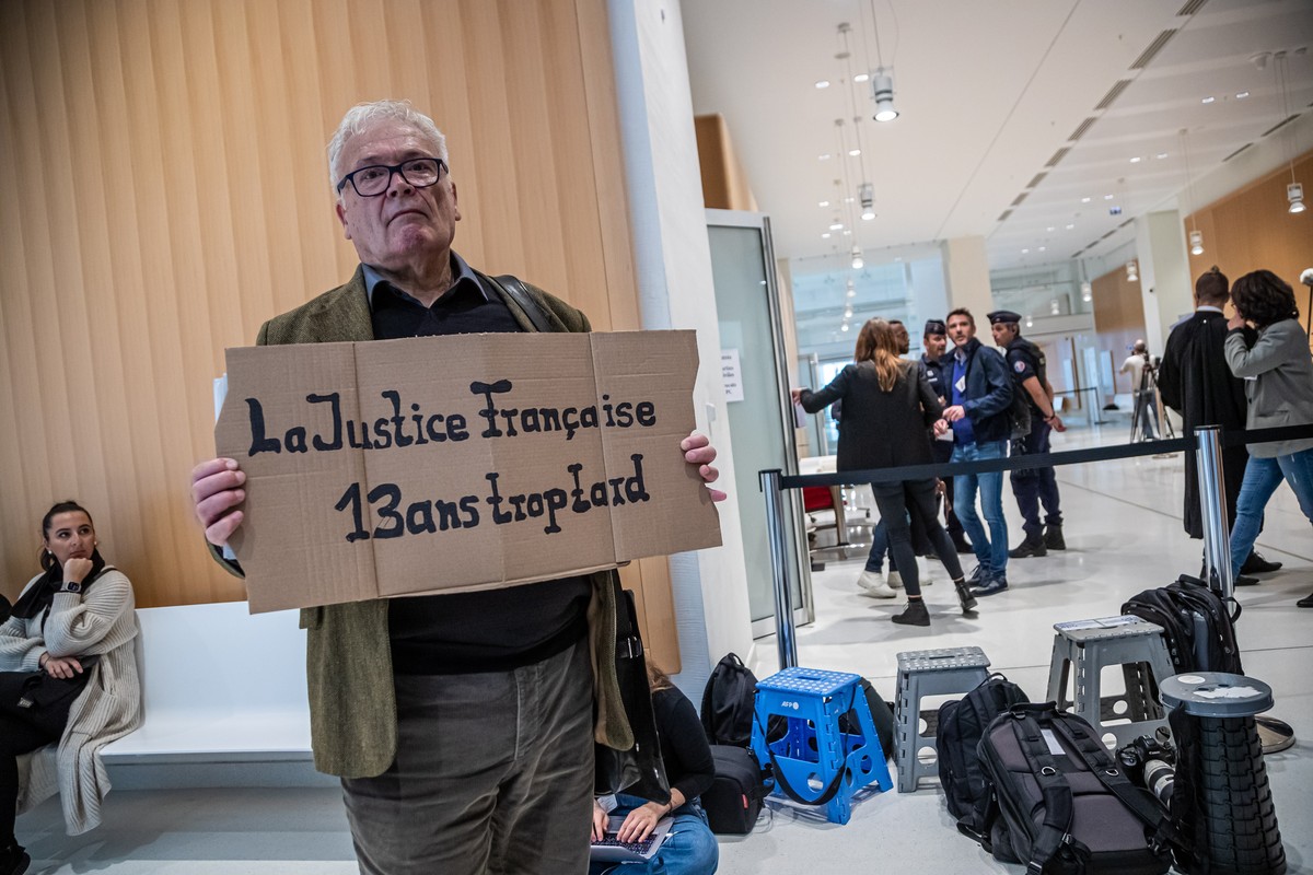 epa10234451 Winfried Schmidt, a relative of German victims holds a poster reading 'French Justice 13 years too late' in front of the courtroom on the first day of the nine-week Rio-Paris fli ...