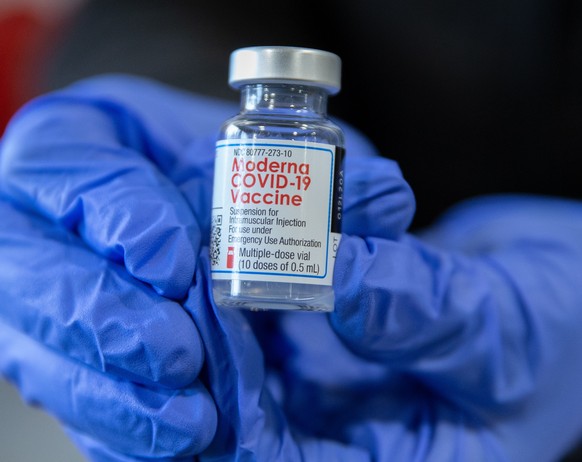 epa08931947 Registerd Nurse Stacey Lane displays a vial of the Covid-19 vaccine shot manufactured by Moderna, after she delivered shots to Police Chief Willam Brooks and Fire Chief George Morrice, at  ...