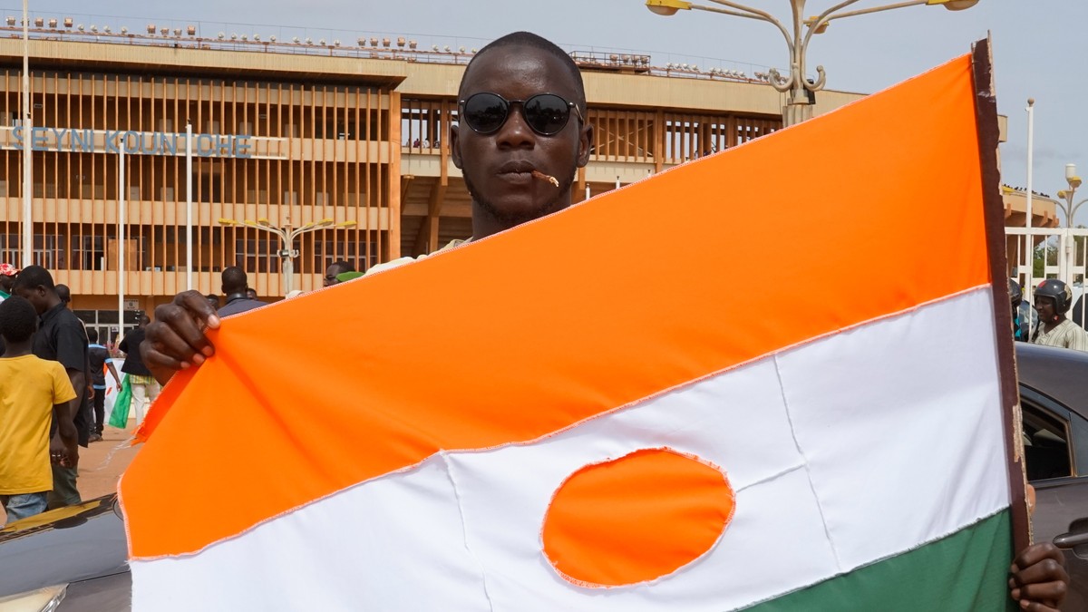epa10788176 A man displays a Niger flag on his way to a rally in a stadium in Niamey, Niger, 06 August 2023. Thousands of pro-junta supporters gathered in a stadium to show their support for the milit ...